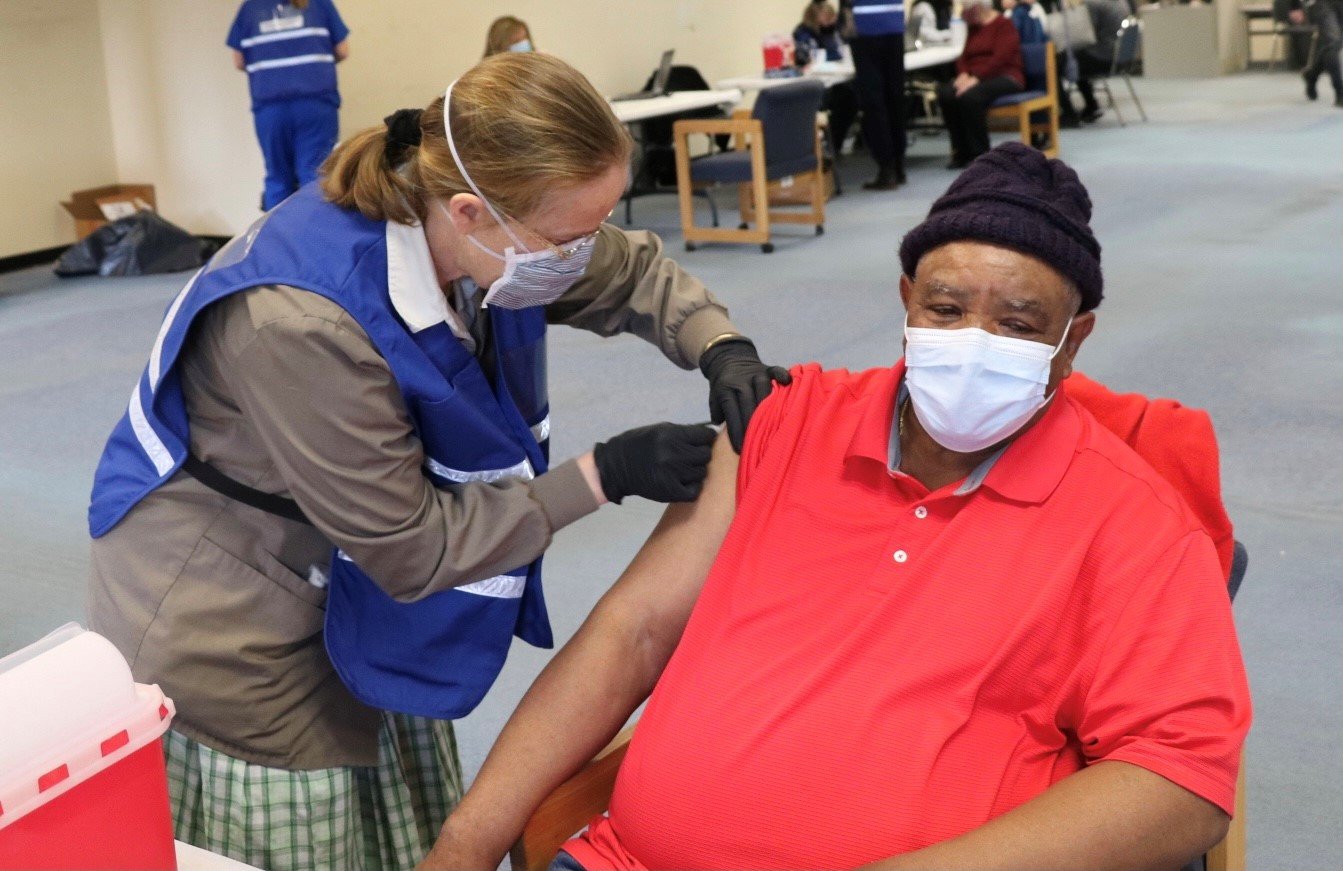 A volunteer nurse from the Bruderhof Community in Walden, administers a vaccination to Middletown’s David Heath, 72