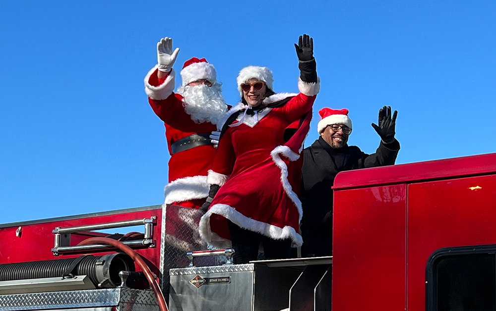 [L-R] Mrs. Claus, Mayor Torrance Harvey and Santa Claus ride atop the fire engine.