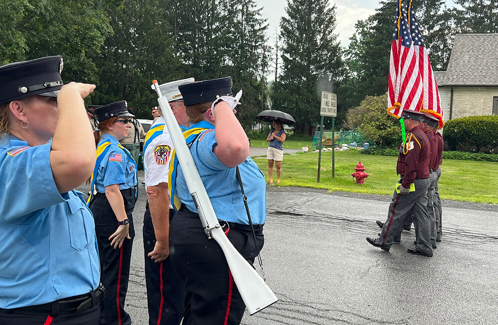 As the rain begins to fall, firefighters salute the colors as they pass.
