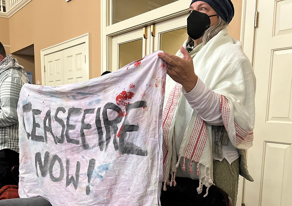 A bedsheet banner displayed at Monday’s City Council meeting urges a more permanent ceasefire in the conflict between Israel and Hamas.